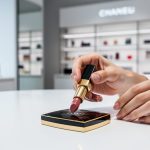 Close-up of a makeup artist’s hands applying lipstick next to a luxury cosmetics compact on a bright vanity in a modern Canadian store.